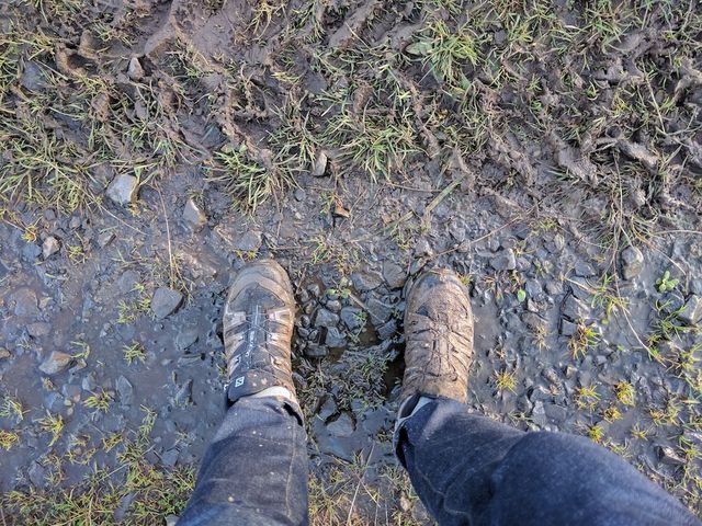 Looking down at hiking boots on a muddy gravel trail in Scotland.
